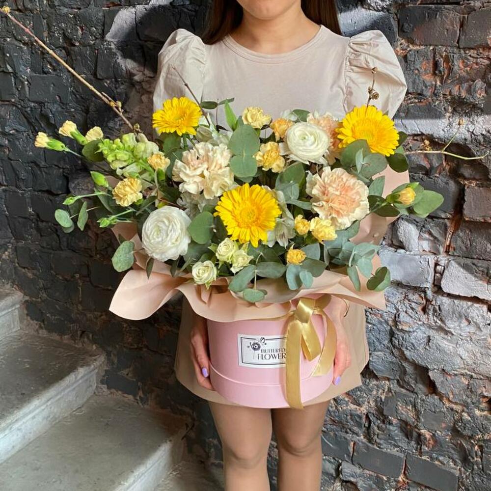 Букет из ранункулюсов, гвоздик, гербер, кустовых роз и эвкалипта в стильной шляпной коробке "Солнце Афин"